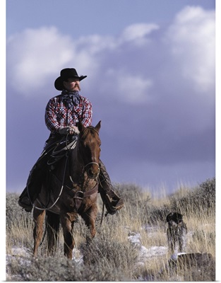 A cowboy poses on his horse with his dog