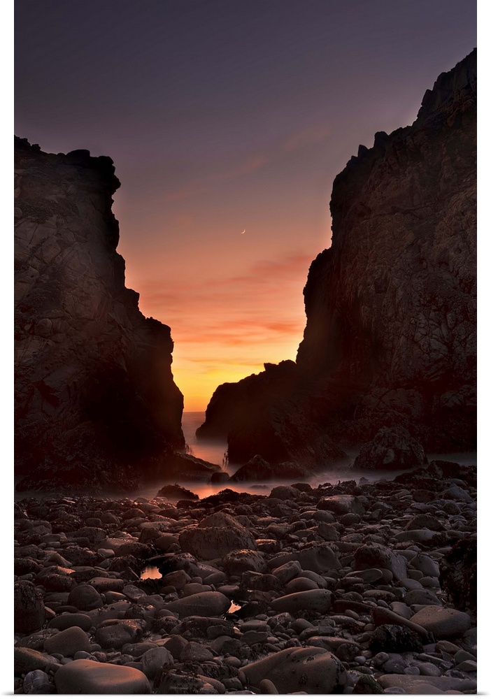 A crescent moon sets through a dusk-colored sky at Pfeiffer Beach, Big Sur, California, USA.