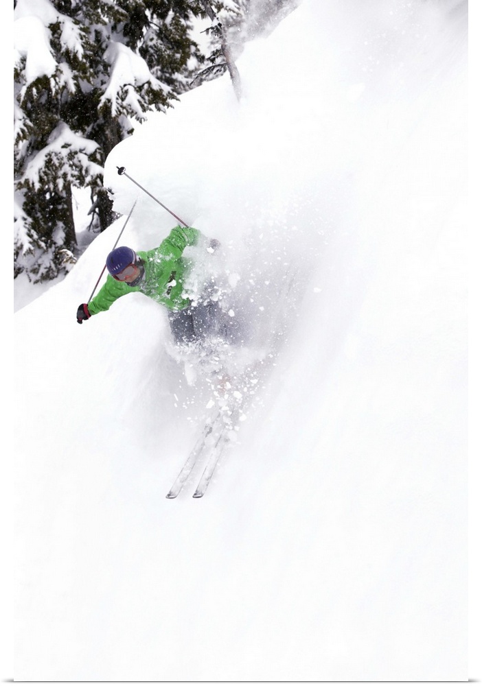 A free skier skis down a steep hill near trees, kicking up snow.
