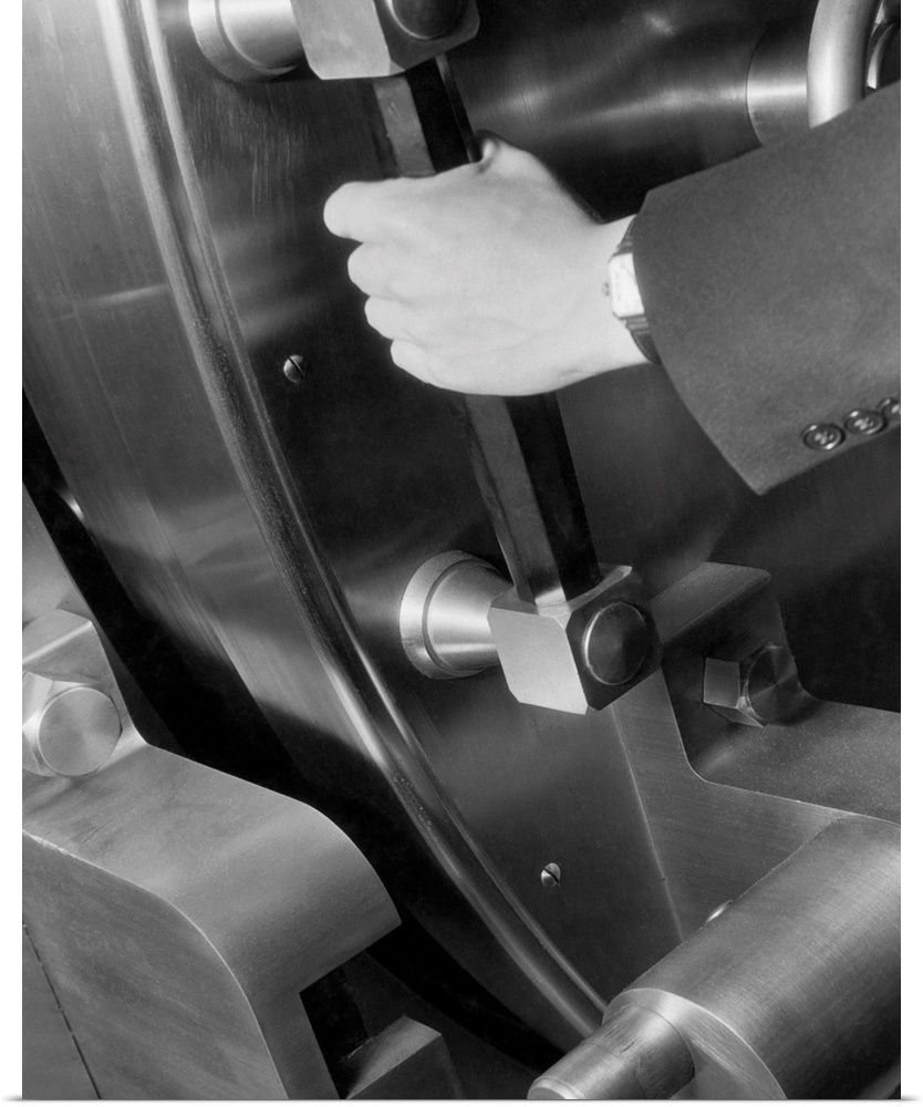 A disembodied hand grasp the handle of a large bank vault and pushes it closed. Undated photograph.