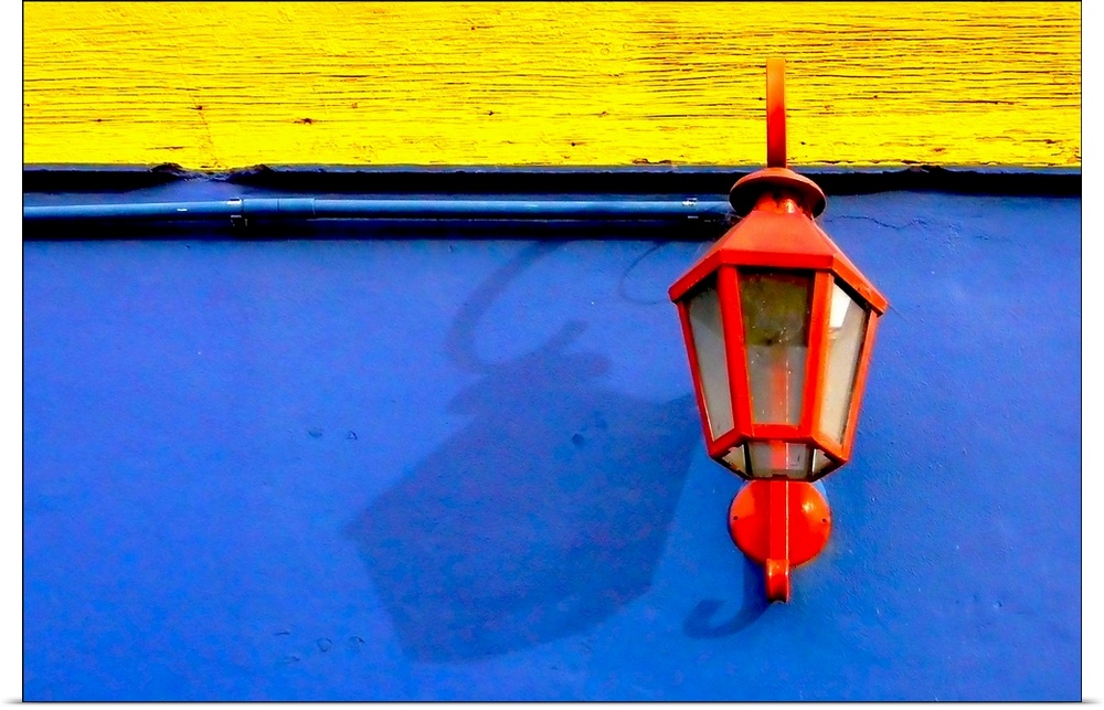 A red streetlamp on a blue and yellow wall.