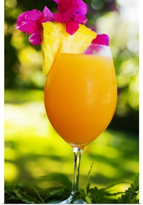 A tropical cocktail garnished with fruit in an outdoor setting.