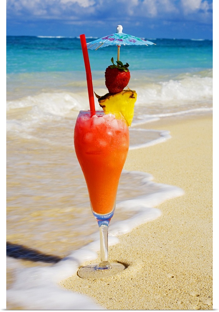 This vertical tropical ocean theme photos show waves washing up on shore around an elaborate drink garnished with fruit.