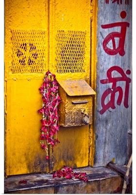 a yellow mailbox is draped with red flowers were left over from a puja