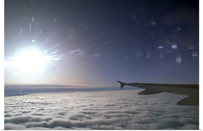 Airplane wing and sun above clouds