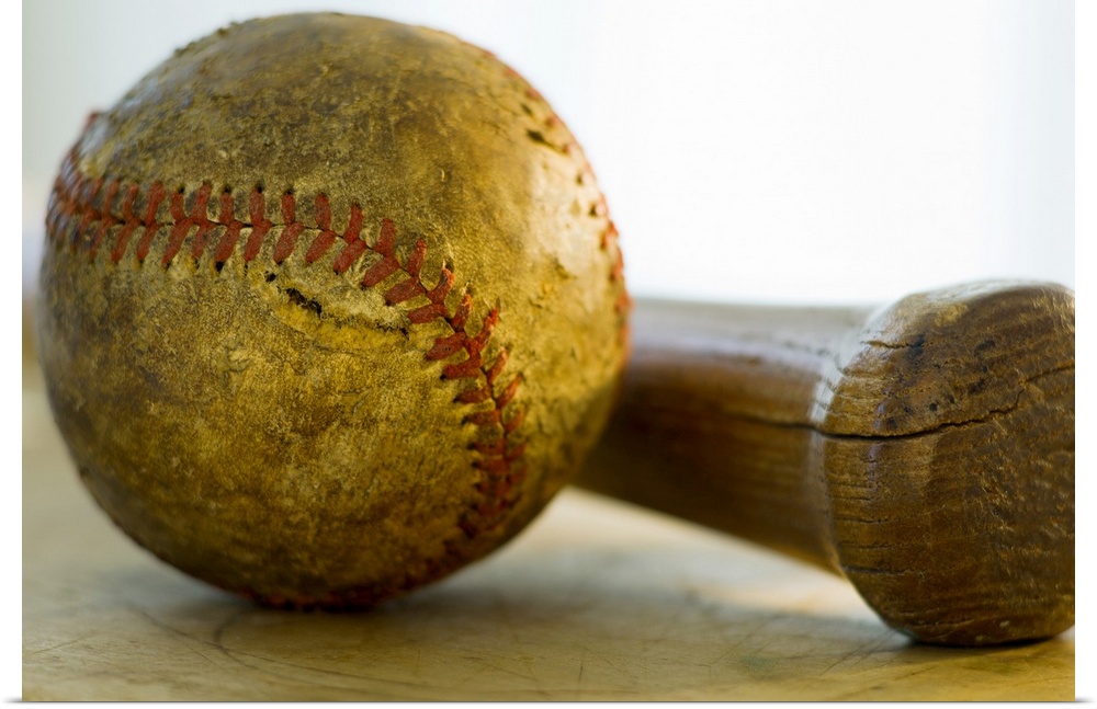 Huge photograph focuses on a stitched ball of worn cowhide sitting next to a wooden hitting instrument on a table.  Both o...