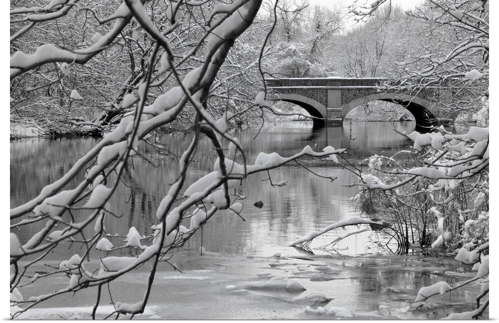 Winter scene of arch bridge over partially frozen river seen trough snow covered branches.