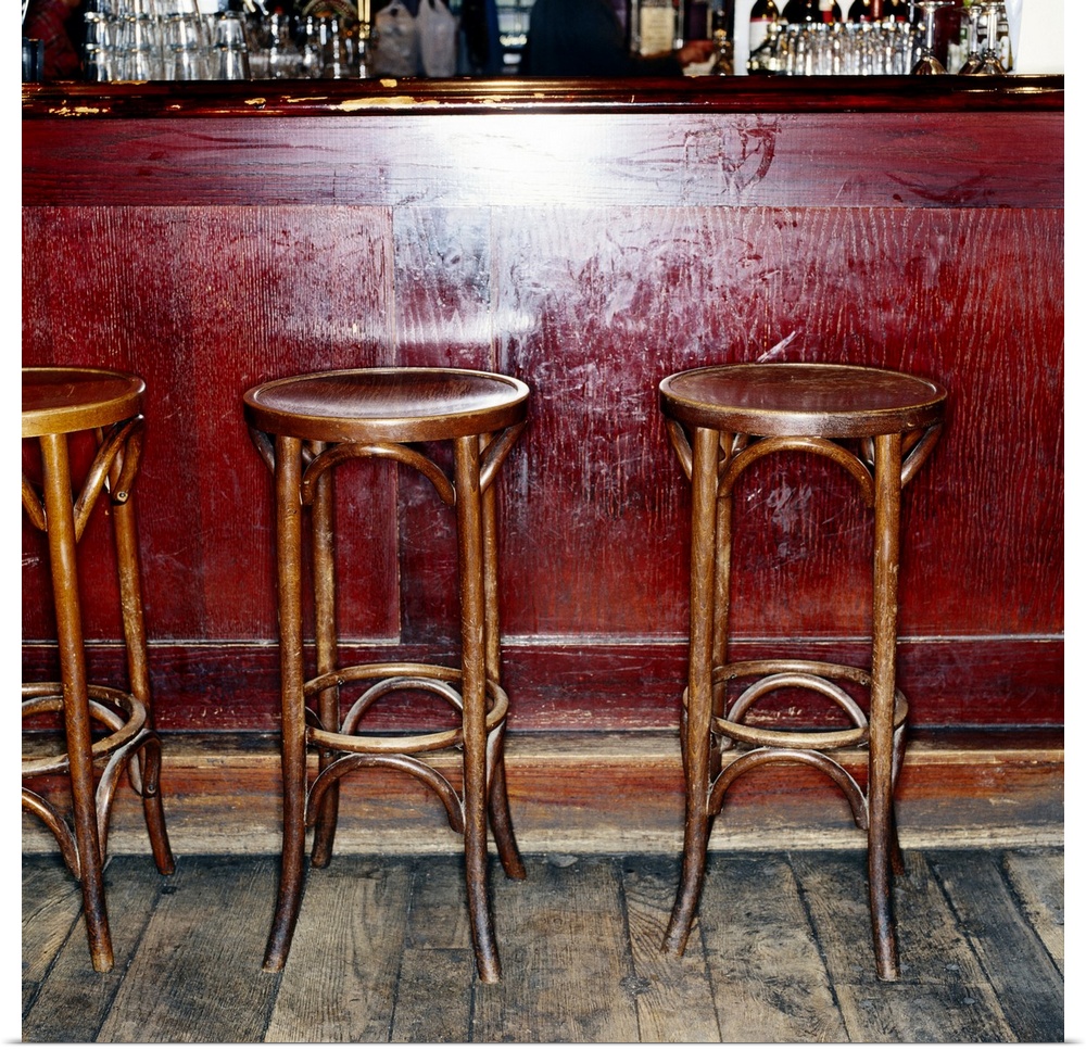 Three tall stools are photographed sitting in front of an empty bar.