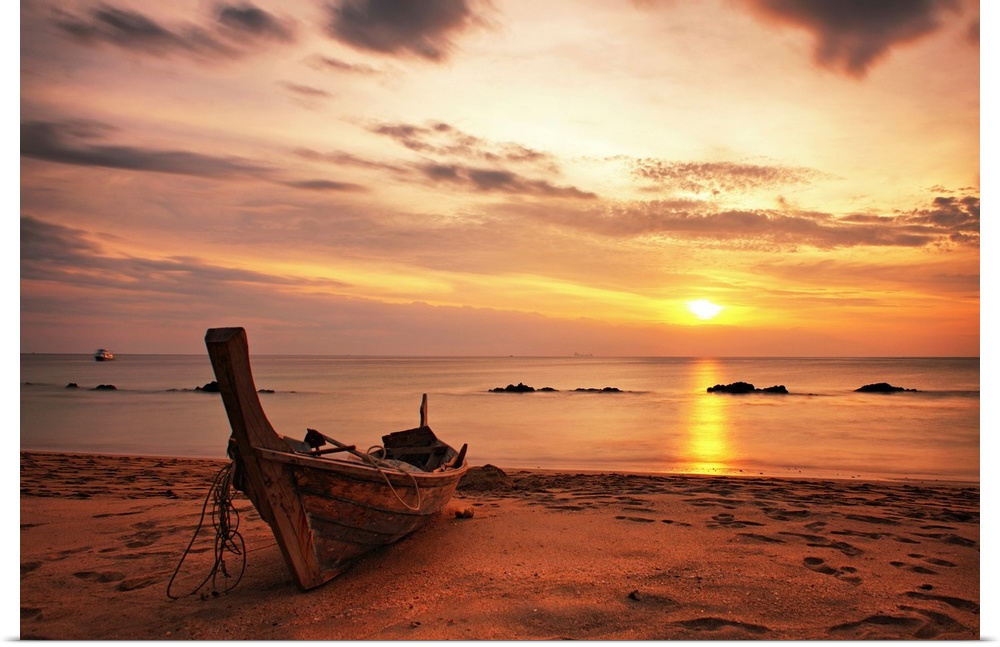 A beautiful picture taken of a wooden boat sitting on the beach as the sun begins to set in the distance.