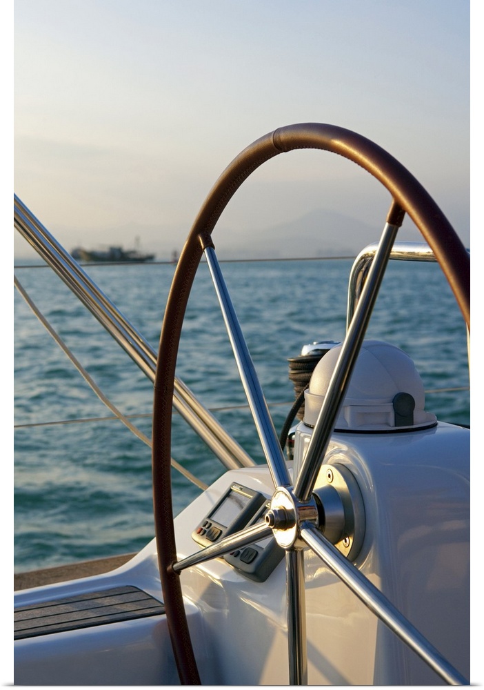 Up-close photograph of steering wheel on sailboat with the ocean in the background.