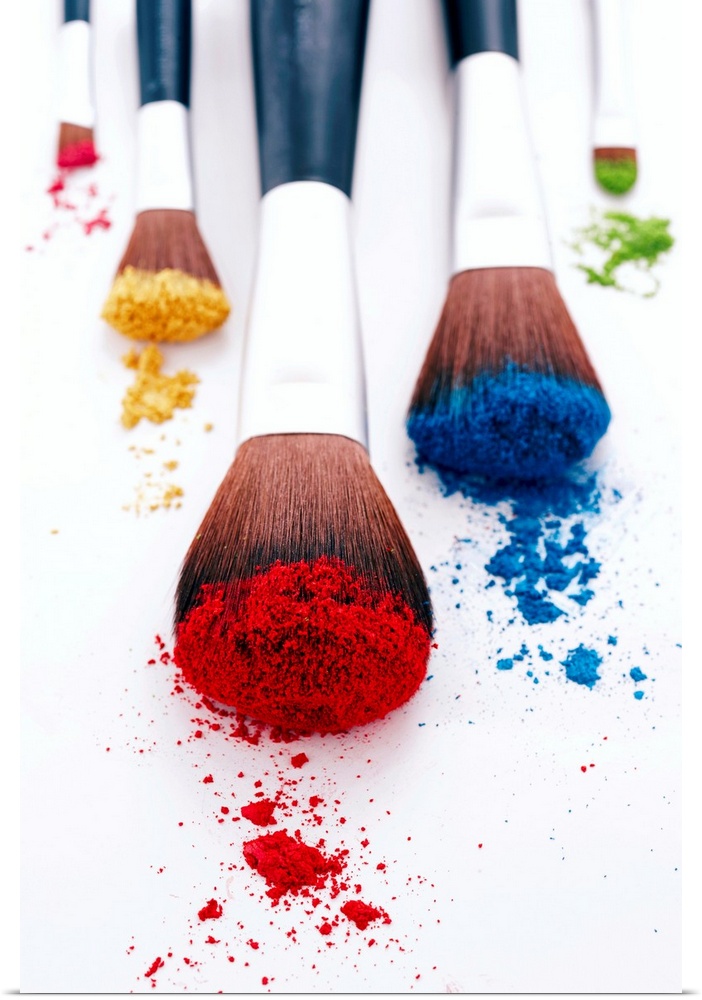 A vertical photo of makeup brushes heavily filled with pigment resting on blank a surface.