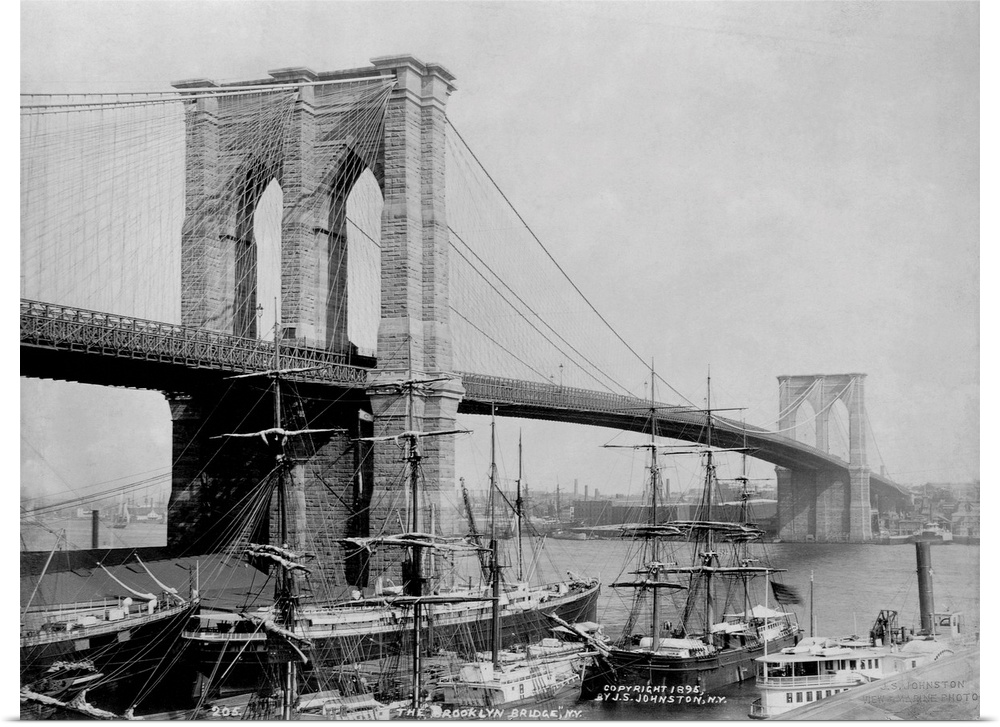 Sailing ships rest in port below the Brooklyn Bridge. The Brooklyn Bridge, designed by John A. Roebling, became the larges...