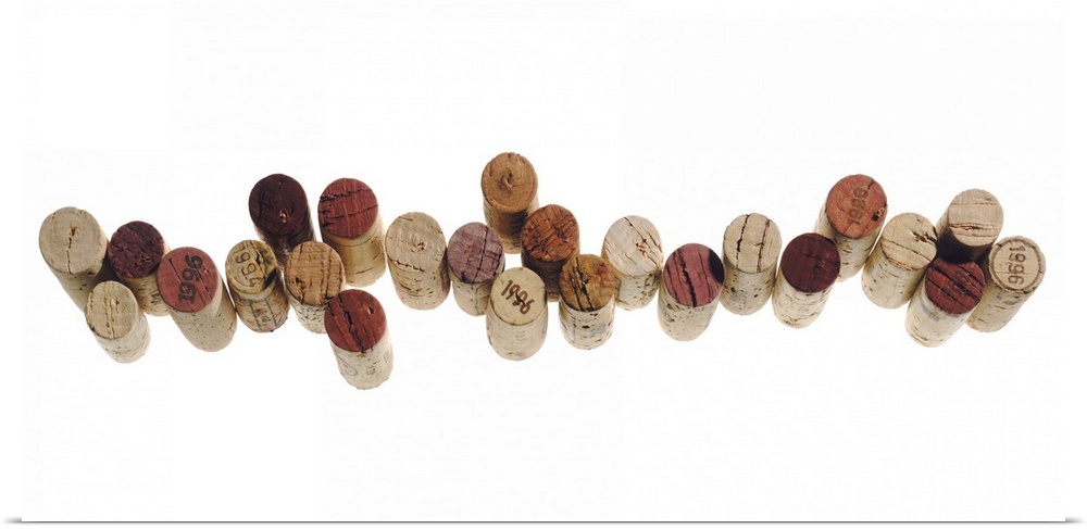 Corks from various wine bottles stand straight up and are lined next to each other on a white surface.