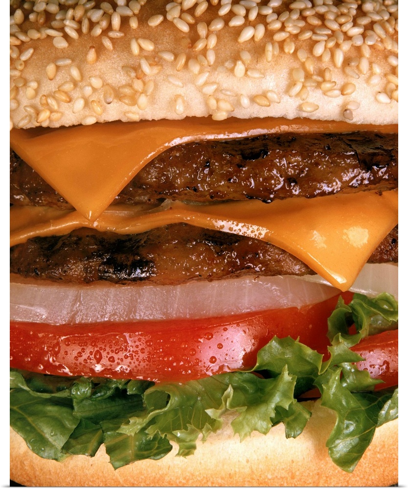 Big vertical close up photograph of a  juicy tow layered cheeseburger with onion, tomato and lettuce on a sesame seed bun.