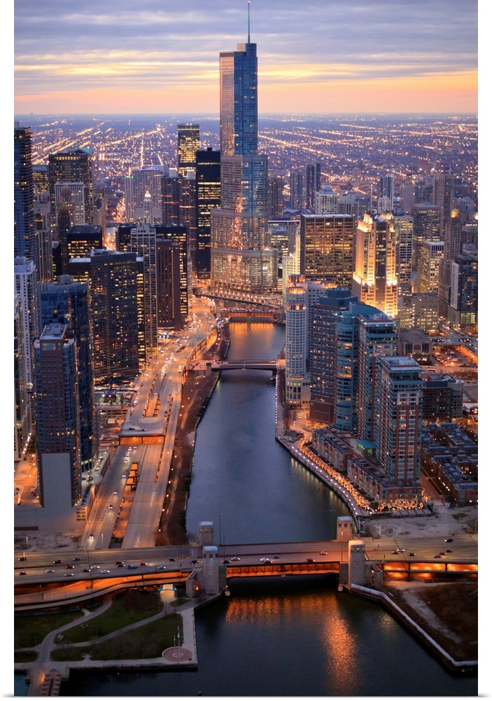Vertical panoramic photograph of city skyline at dusk.  Building lights are shining and there is a river running through t...