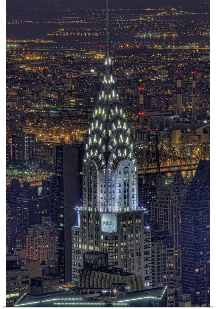 Aerial vertical picture of the top of the Chrysler building lit up at night with the rest of downtown New York lit up in t...