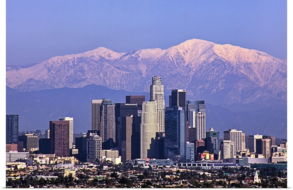 This large piece is a photograph large buildings in Los Angeles with big snow covered mountains in the backdrop.