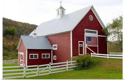Classic New England farm with red barn and white fence, American flag on barn door