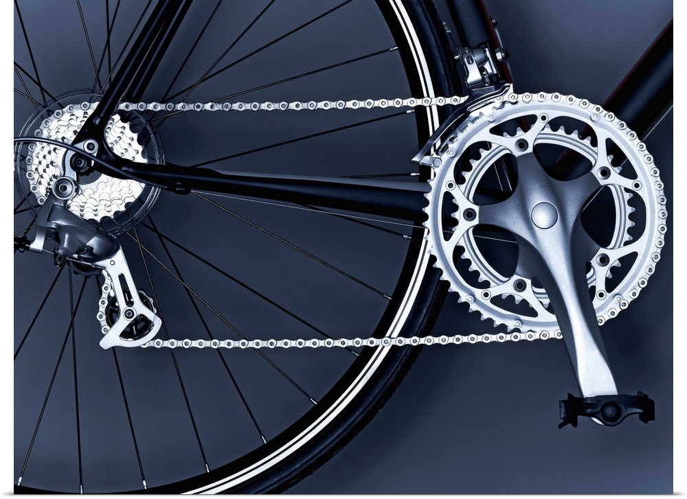 Oversized, horizontal, close up photograph of part of the back wheel, the chain, gears and pedal of a black bicycle.