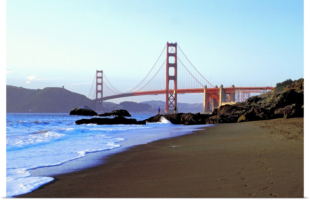 Landscape photograph looking down the rocky shoreline toward the Golden Gate Bridge, beneath a blue sky, in California.