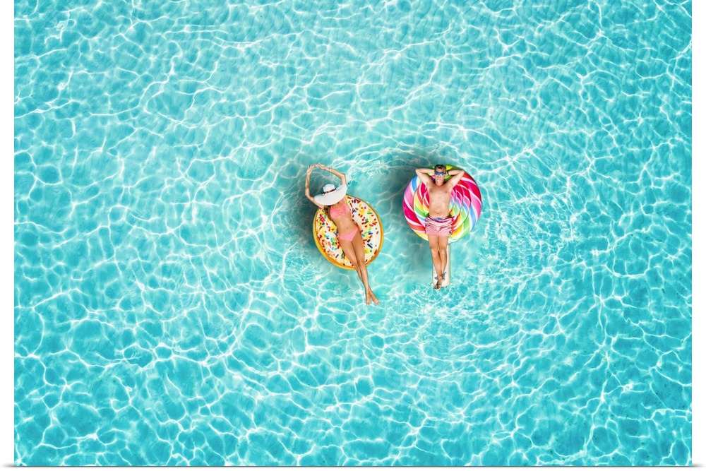 A happy vacation couple in swimsuits enjoys the tropical sun of the Maldives on colorful floats over turquoise colored sea.