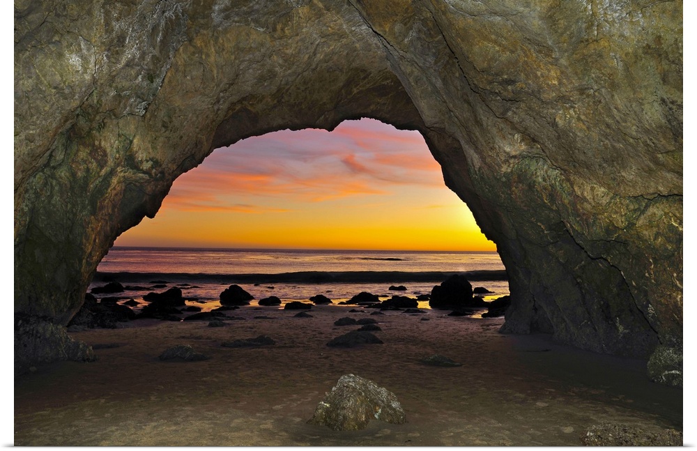 Dramatic sunset seen from inside cave on beach.