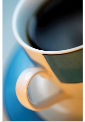 Extreme close-up of cup of black coffee in tan and black cup with blue saucer