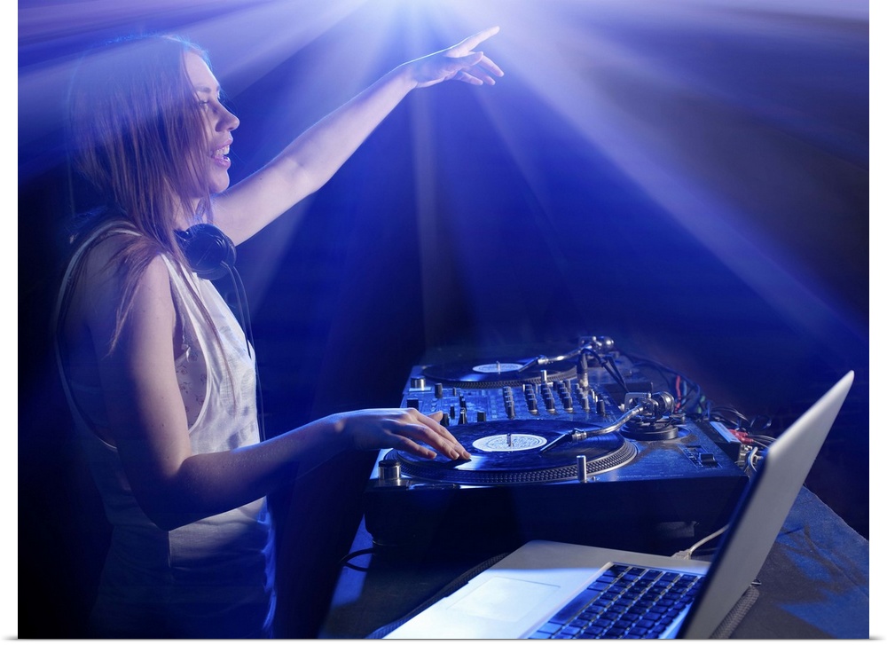Female DJ using decks and laptop, reaching out to audience, surrounded by bright lights