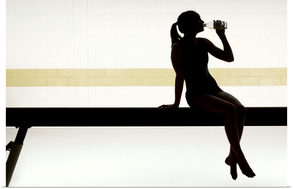 Female gymnast sitting on balance beam drinking water