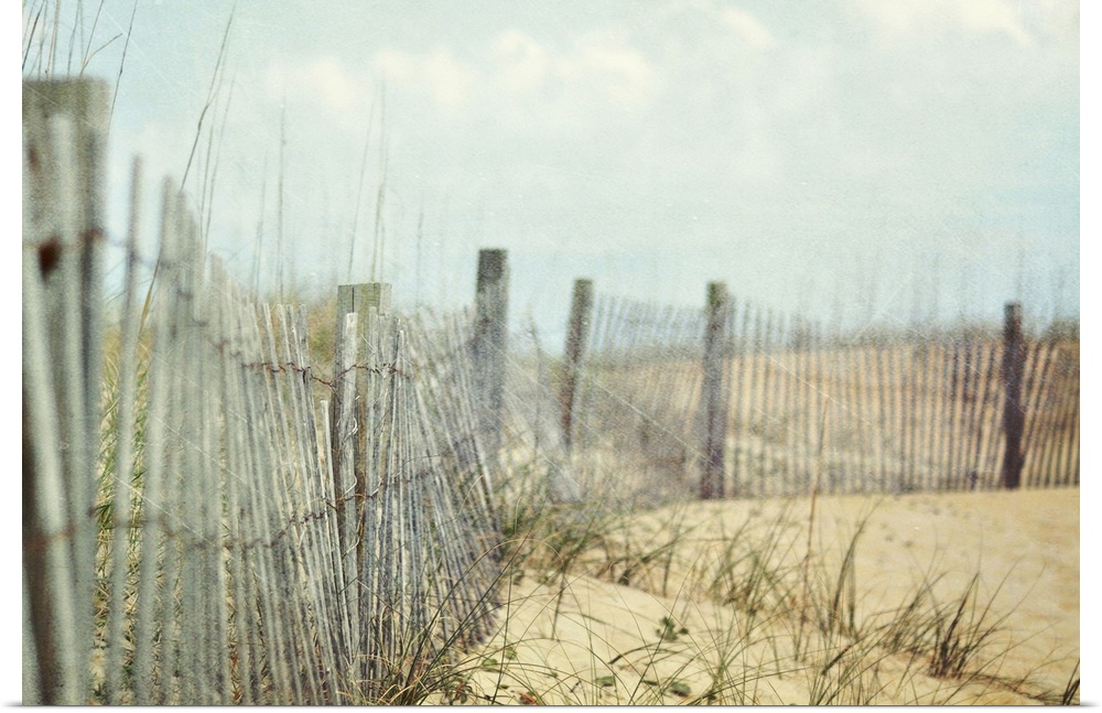 Photograph of wooden fence and tall grass on hills of sand at the coast under cloudy skies.