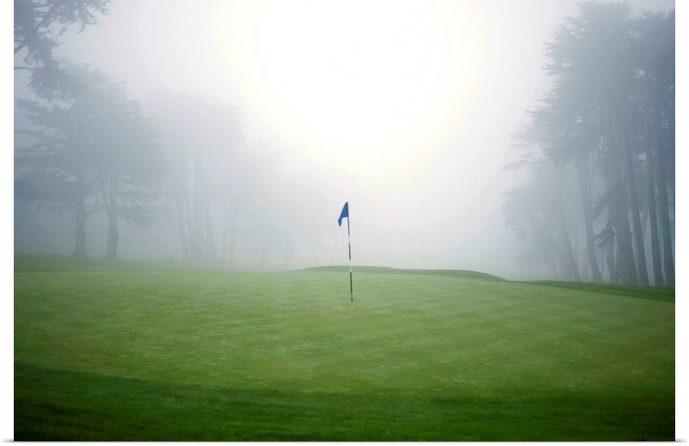 Flag on putting green on golf course, fog and trees in background