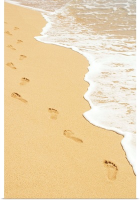 Footprints in sand walking next to foamy ocean edge
