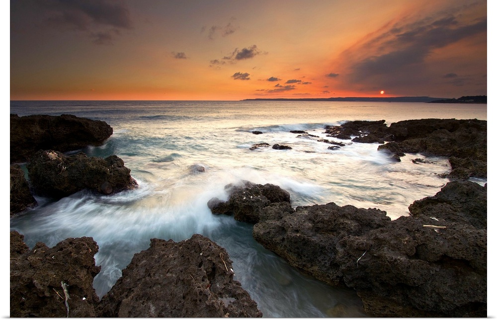 Frog Rock, kenting at dusk with foaming waves rushing in and crashing on dark coral reefs while sky is painted red by sett...