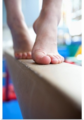 Girl slowly walks across balance beam on her toes, close up of feet