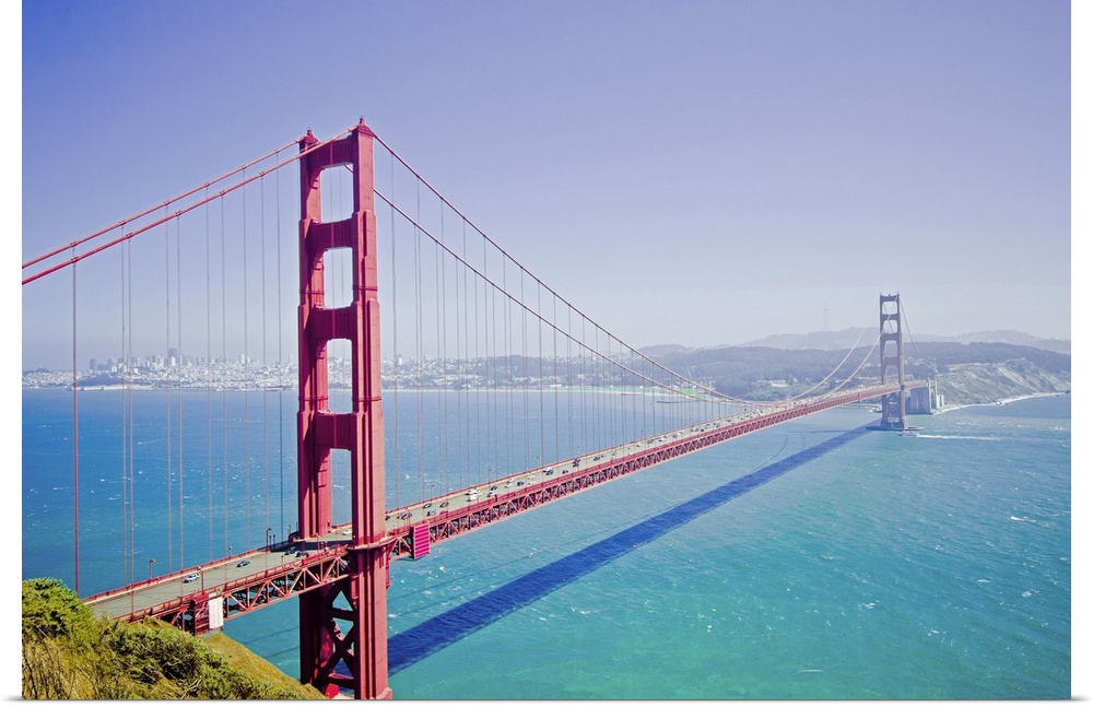 A high angle photograph is taken of the Golden Gate bridge on a bright sunny day with a soft haze over the entire picture.
