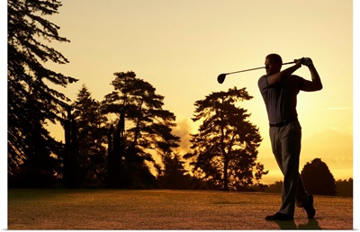 Golfer swinging club on golf course at sunset
