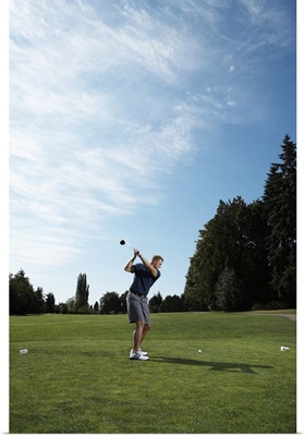 Golfer swinging club on golf green, side view