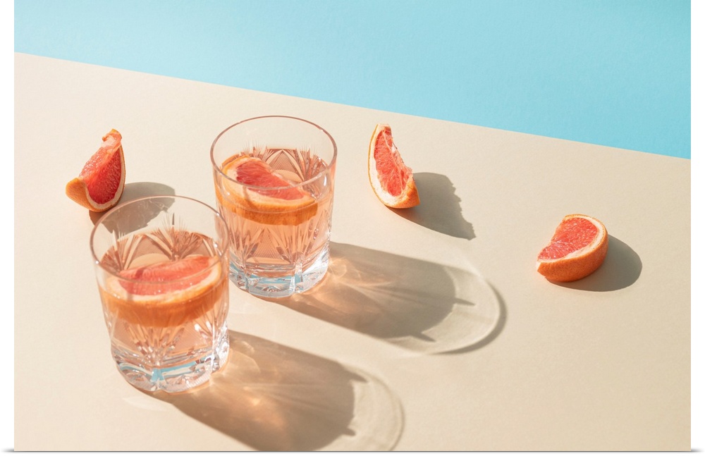 Two drink glasses with slices of fresh grapefruit against a bright beige and blue background.