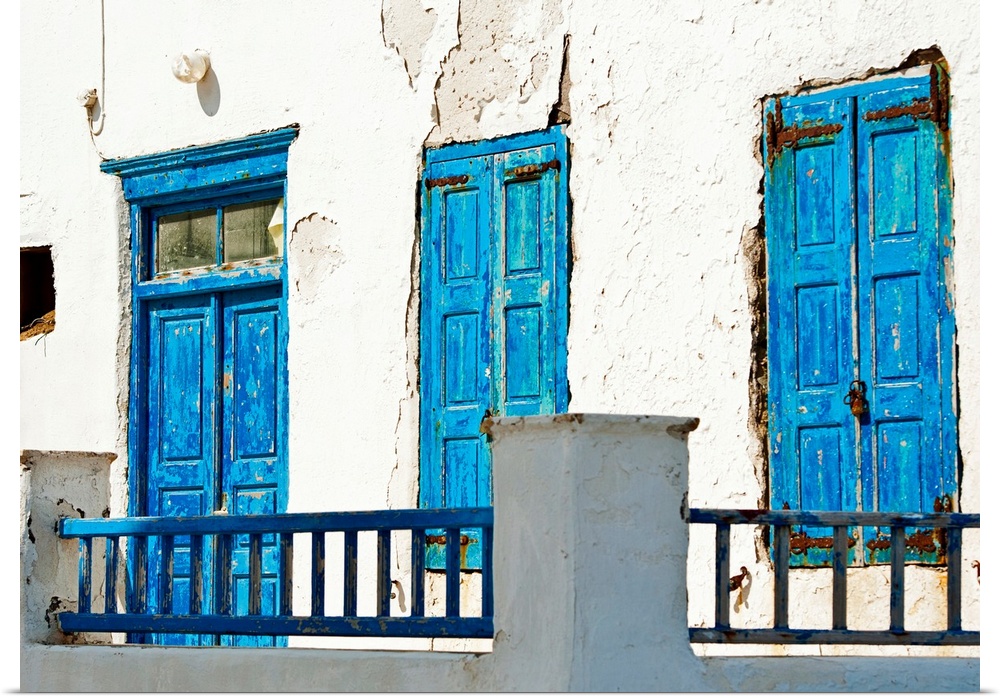 Photograph of brightly-painted distressed doors against a stark, white wall on the Cycalades Islands in Mykonos, Greece.