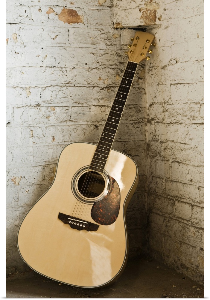 Large, portrait photograph of an acoustic guitar leaning in the corner of an old, rough, painted brick wall.