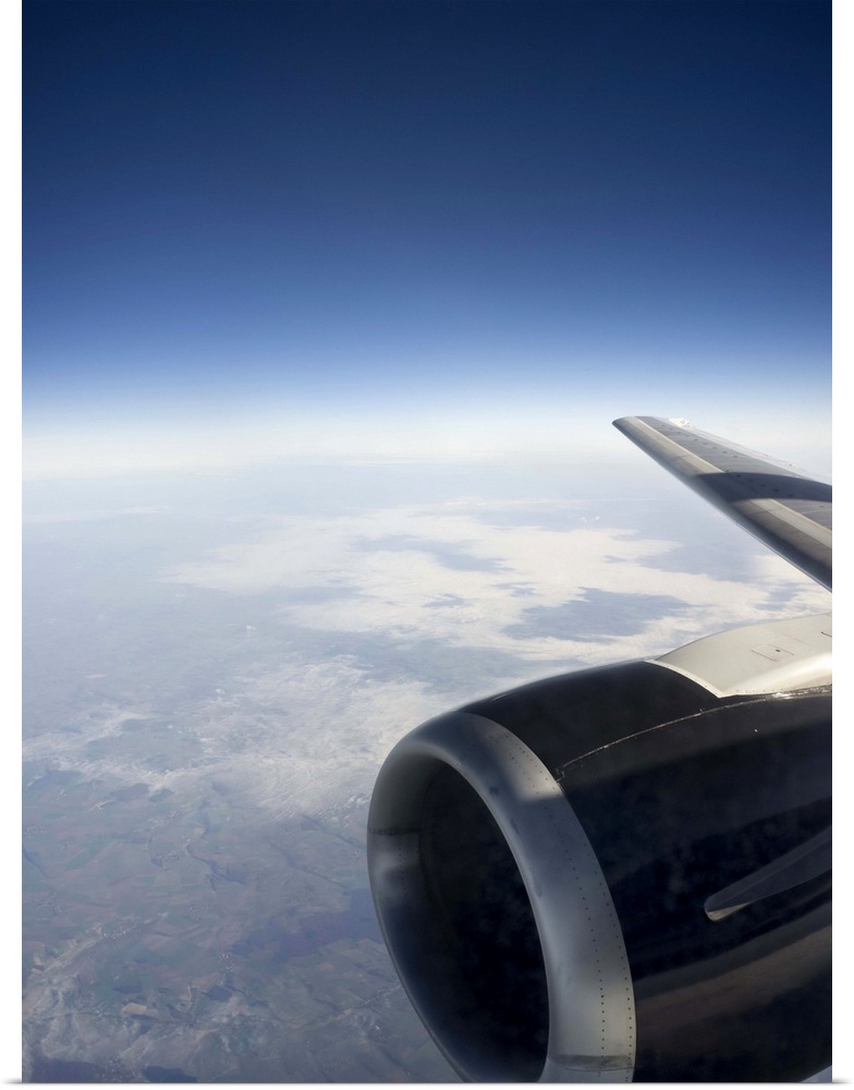 High altitude view of a jet engine set against a gentle cloudscape with the outline of land and coastline visible beneath ...