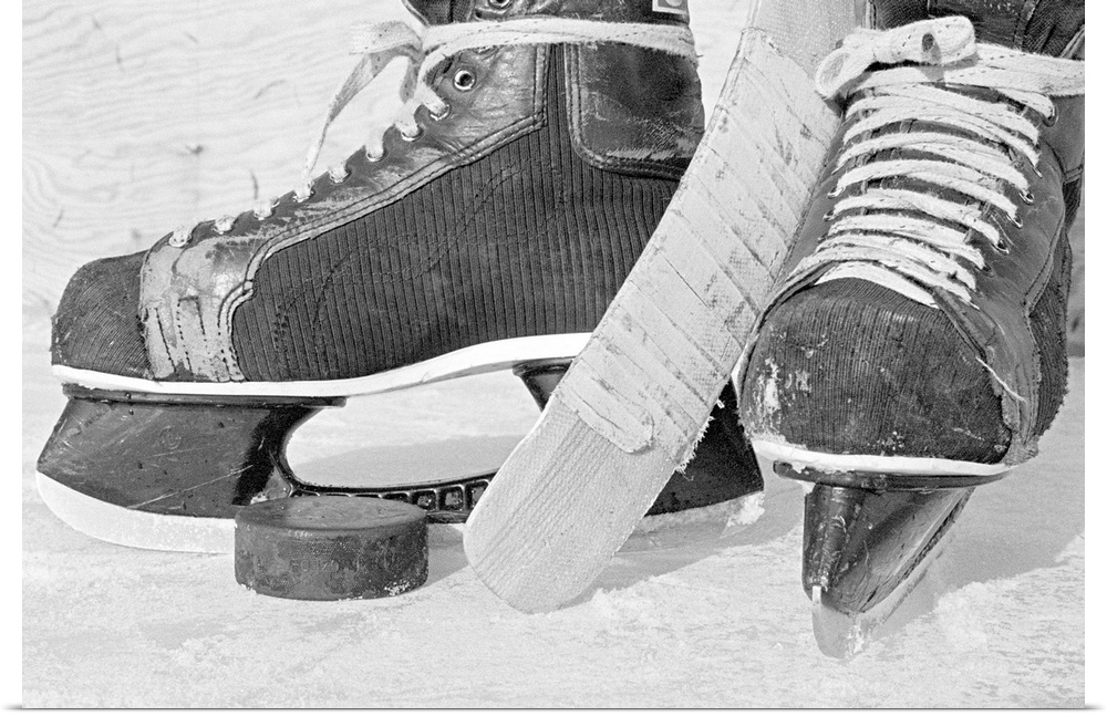 Large, landscape photograph of vintage hockey skates on the ice.  Between the skates is the end of a stick and a hockey puck.