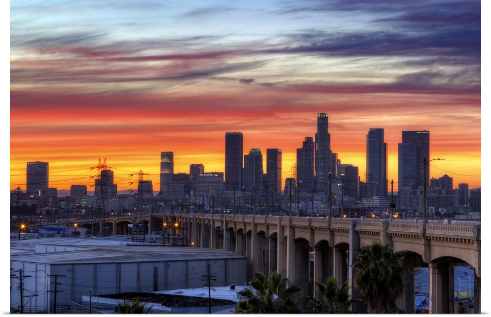 Sunset creates a stunning display on the cloudy sky over a California cityscape with skyscrapers and a bridge.