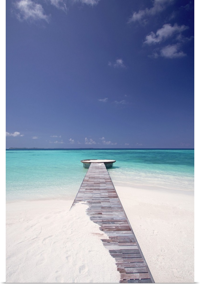Vertical photo of a wooden walkway stretching out into the tropical sea, partly covered in sand.