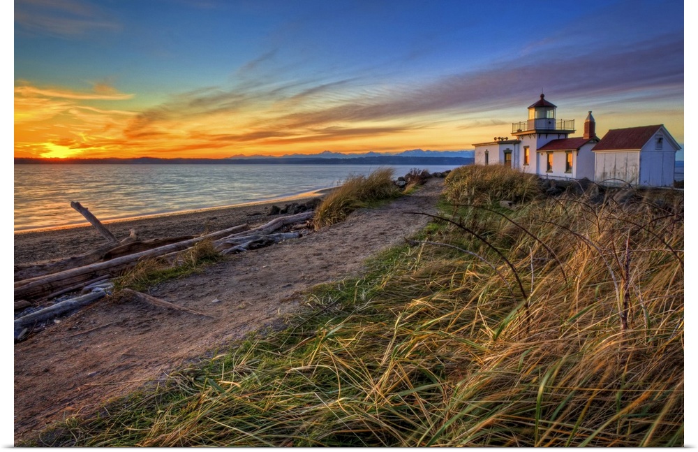 Oversized, landscape, angled photograph of a coastline in Washington at sunset, with a lighthouse in the background.