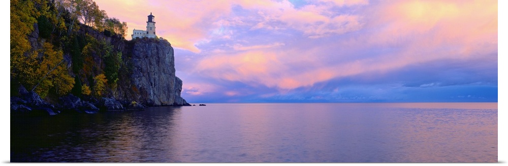 Panoramic photo print of a lighthouse on top of a cliff overlooking the water at sunset.
