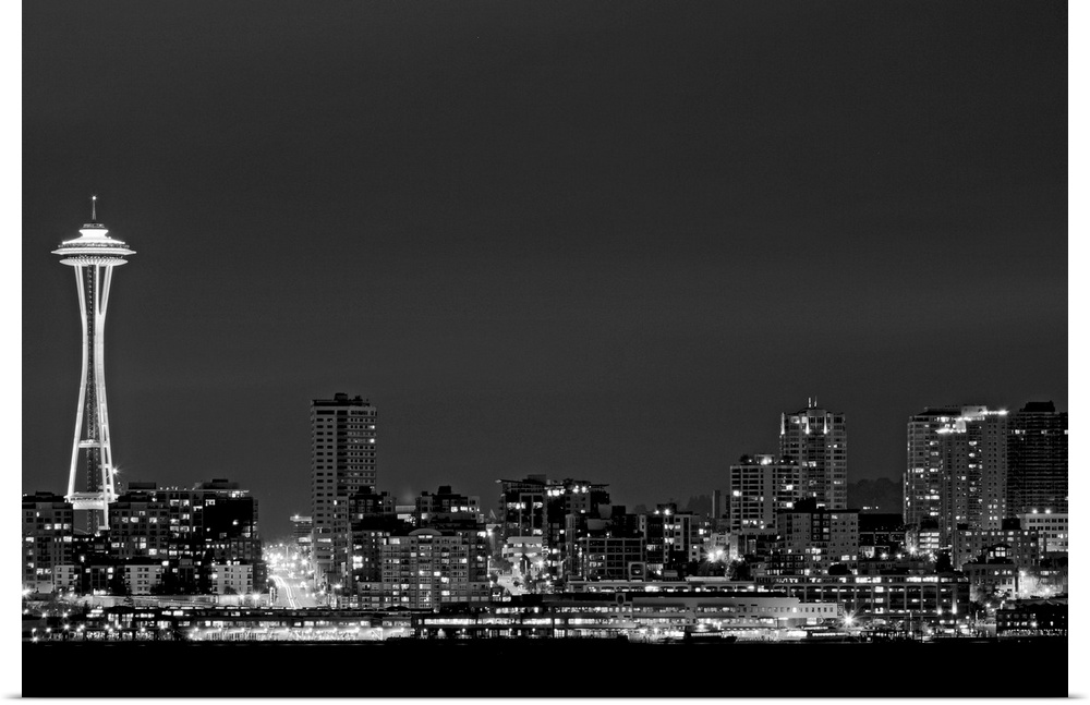 Black and white photograph taken of the city skyline in Seattle with the city illuminated under a night sky.
