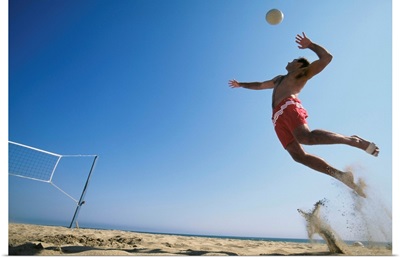 Male beach volleyball player jumping up to spike ball