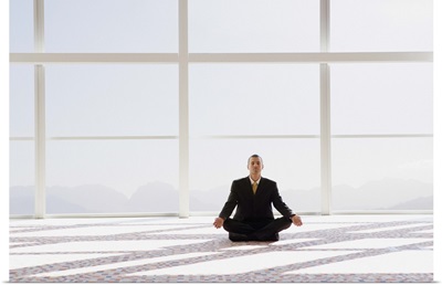 Man meditating, sitting cross-legged in office, eyes closed