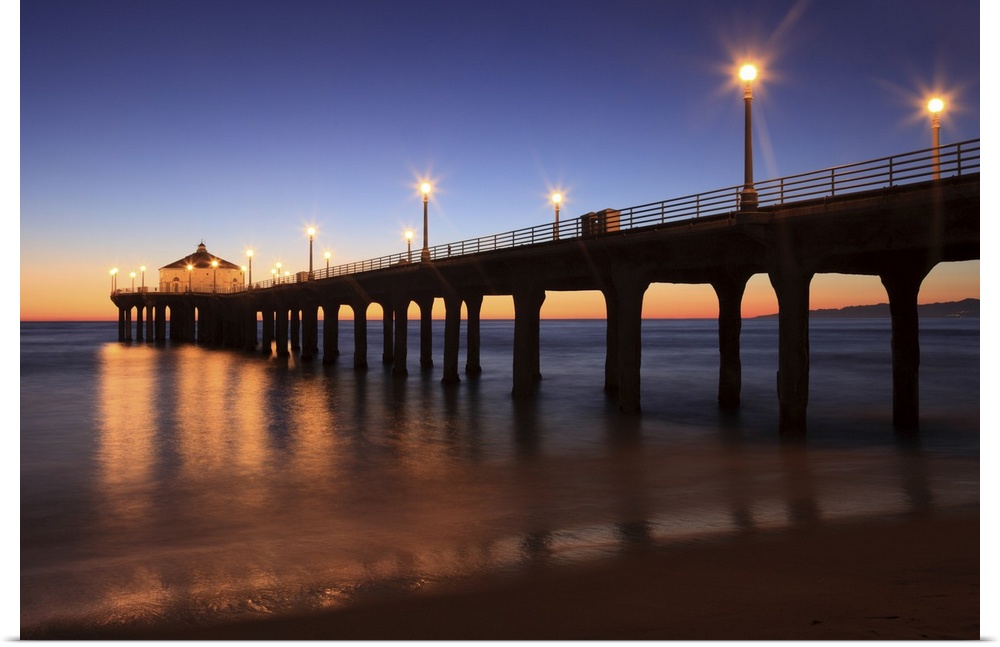 Big canvas print of a pier that is silhouetted against a sunset with lights lit up along it.